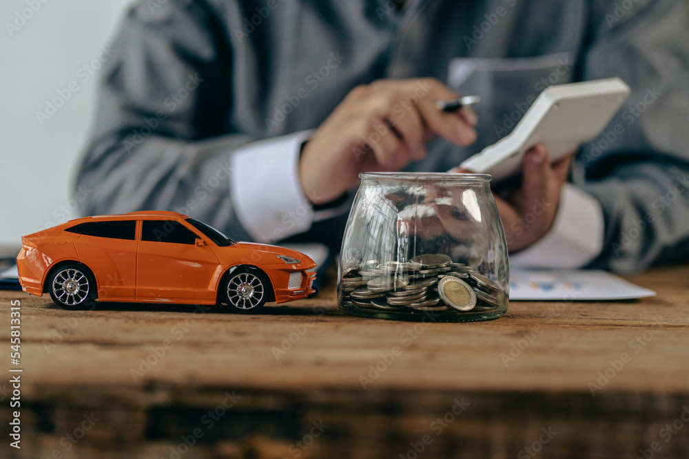 Piggy bank and toy car house on the table with man as background, money saving concept for paying for the car, house.