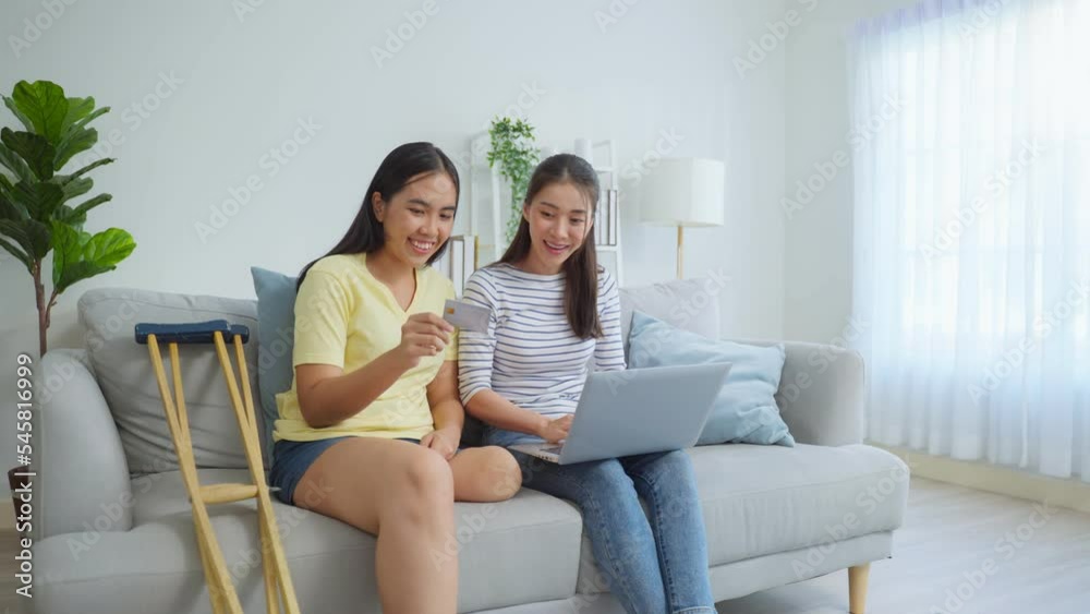 Asian woman amputee using laptop computer with friend in living room. Asian woman amputee using laptop computer with friend in living room.