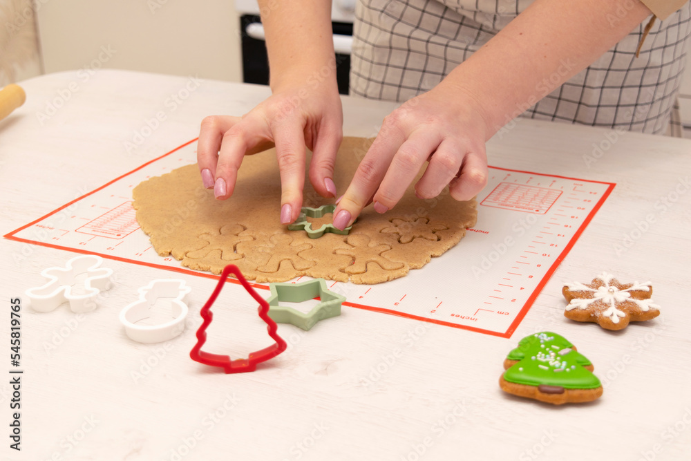 Obraz premium Caucasain woman rolls out the dough with a rolling pin and cuts cookies with cookie cutters at the kitchen