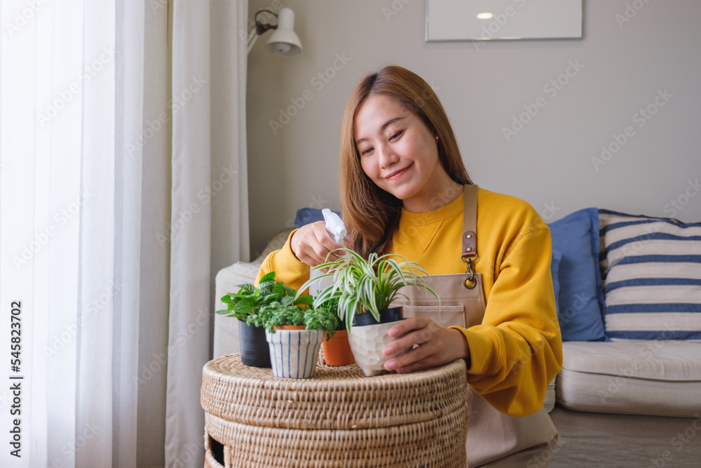 Portrait image of a beautiful young woman taking care and watering houseplants with plant mister spray at home