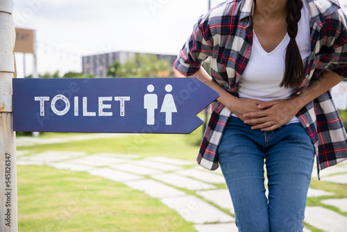 Bowel incontinence pain. Woman hand holding crotch near sign toilet in the park. Finding location for ease