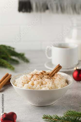  Scandinavian rice porridge with cinnamon in a bowl surrounded by Christmas balls. Breakfast on Christmas Eve.