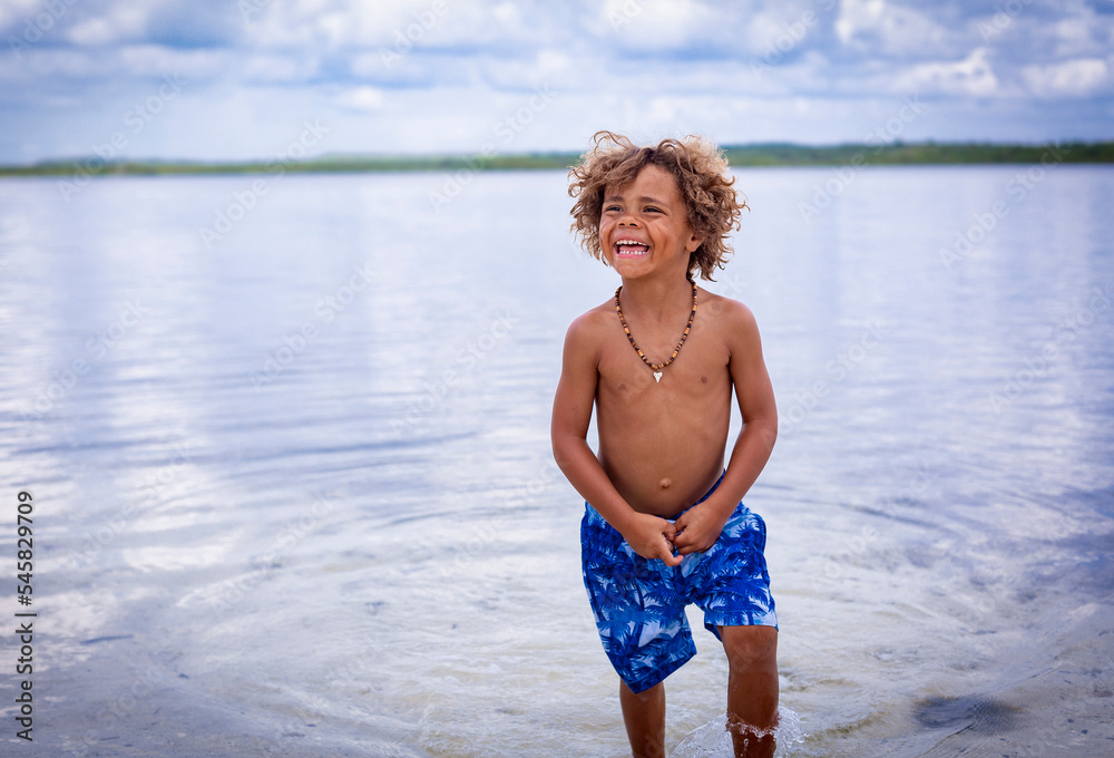 Candid portrait of one cool kid hanging out in a swimsuit on the beach smiling and having a great time. African American boy living his best life
