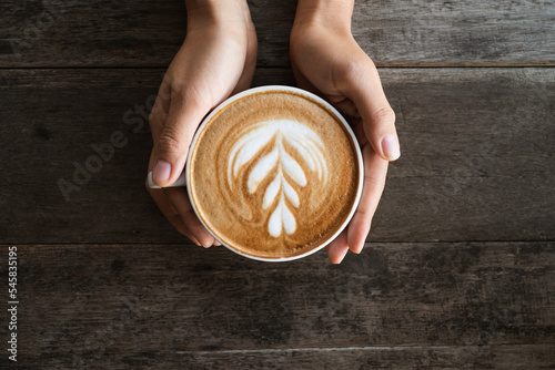 Latte art coffee with heart tree shape in coffee cup holding by hand on wooden background, Hot drink, Table top view