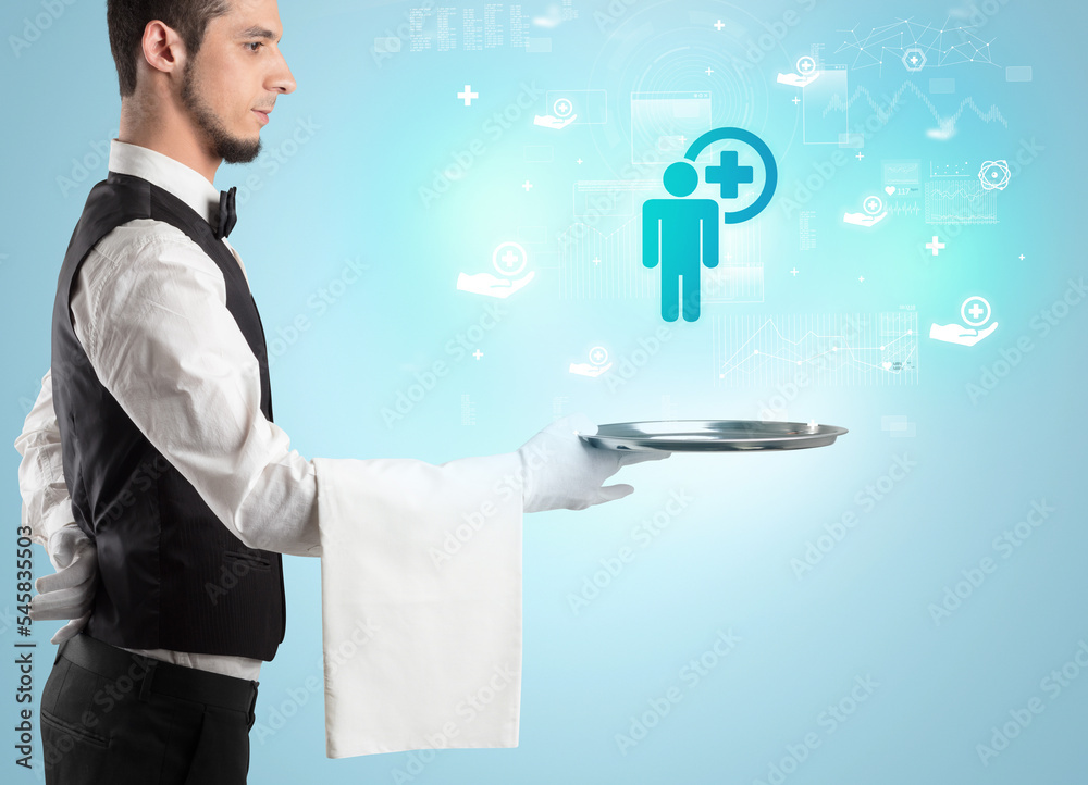Handsome young waiter in tuxedo holding healthcare icons on tray Handsome young waiter in tuxedo holding healthcare icons on tray