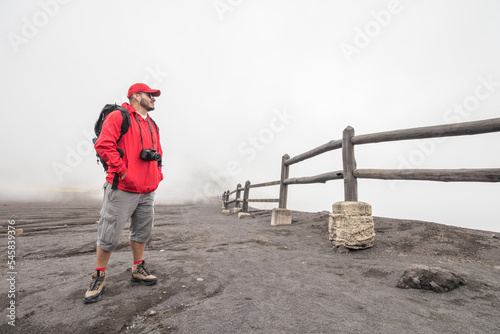 hiker with cap and waterproof jacket contemplating the viewpoint surrounded by fog in the Irazu Volcano National Park photo