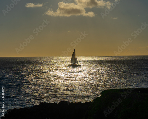 A single mast sailboat crossing the sun glitter pattern creating a  silhouette against the afternoon sky, Poipu, Kauai, Hawaii © Ron