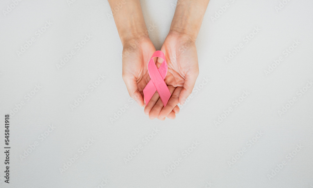 Woman's hands holding pink ribbon on white cloth background. Symbol of breast cancer awareness campaign. Healthcare concept Woman's hands holding pink ribbon on white cloth background. Symbol of breast cancer awareness campaign. Healthcare concept