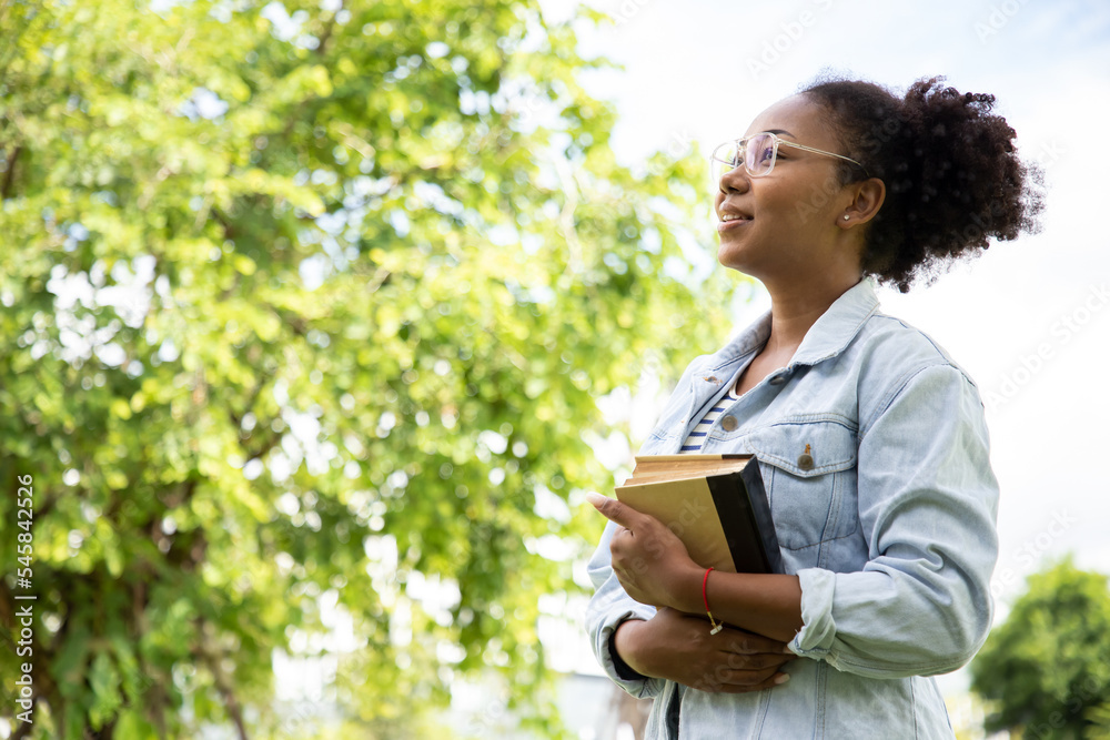 Smiling charming African American woman in imagined dreaming and happiness after reading the favorite book during the travel on the sunny tree. Smiling charming African American woman in imagined dreaming and happiness after reading the favorite book during the travel on the sunny tree.