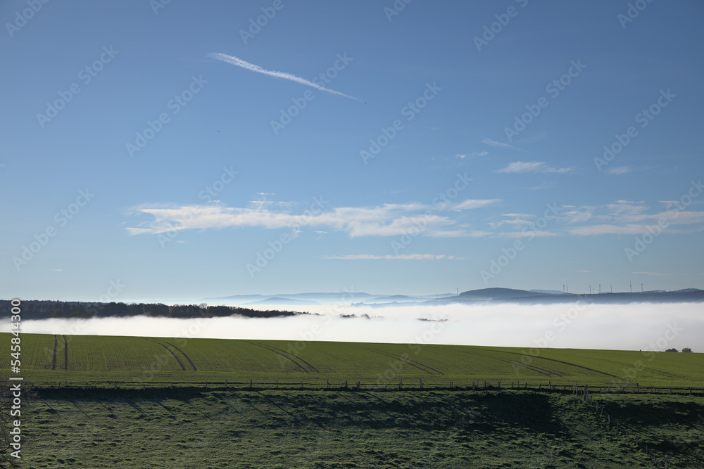 Wide landscape in the morning with fog in the valleys blue sky, a fence and green meadows