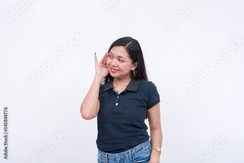A friendly asian woman requesting to listen on the latest gossip. Hand gesture on ear. Isolated on a white background.