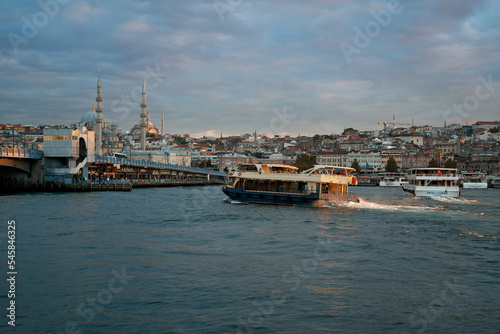 A large tourist boat floats on the river in the rays of the setting sun, against the backdrop of a Turkish city, with a beautiful mosque.