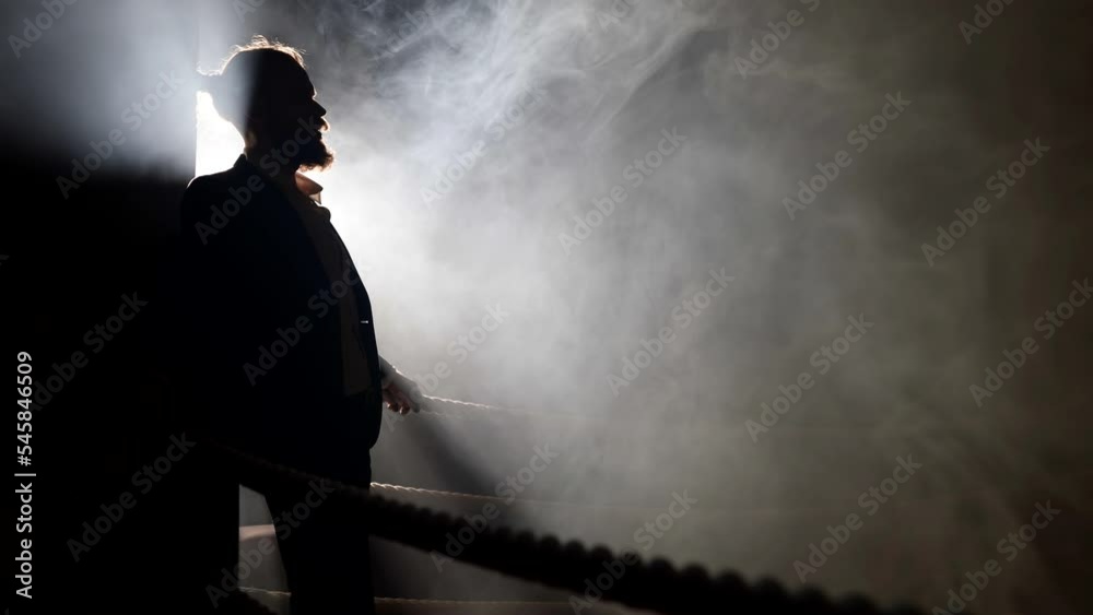mysterious bearded man in business suit on box ring in darkness, silhouette of adult man mysterious bearded man in business suit on box ring in darkness, silhouette of adult man