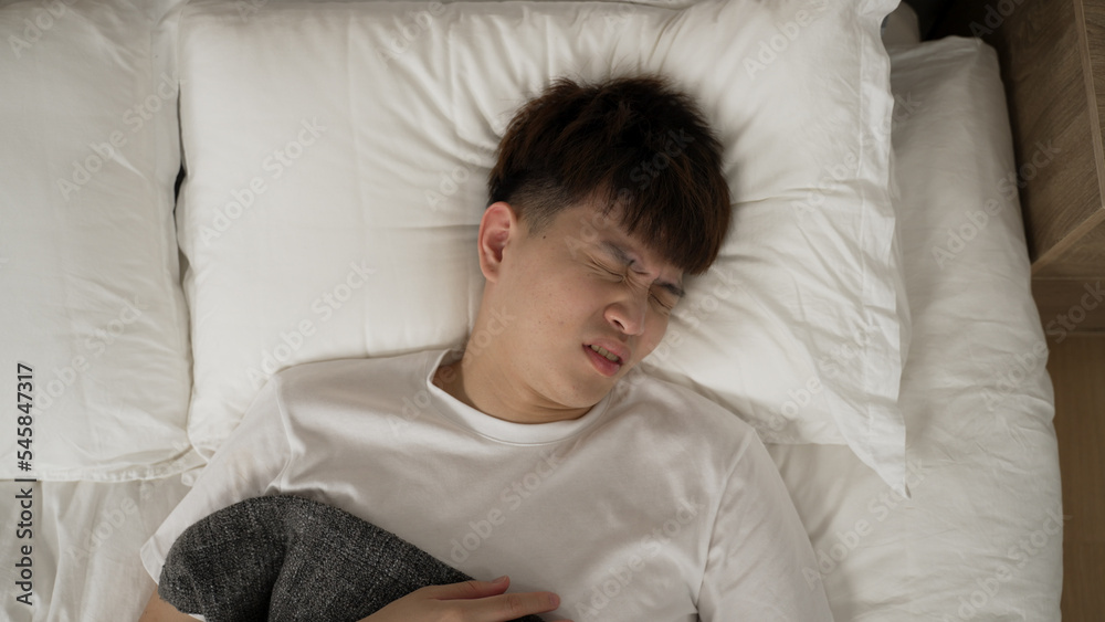 view from top of stressed asian man face grimacing due to nightmare and waking up touching his chest feeling scared while trying to catch breath on bed in the bedroom view from top of stressed asian man face grimacing due to nightmare and waking up touching his chest feeling scared while trying to catch breath on bed in the bedroom