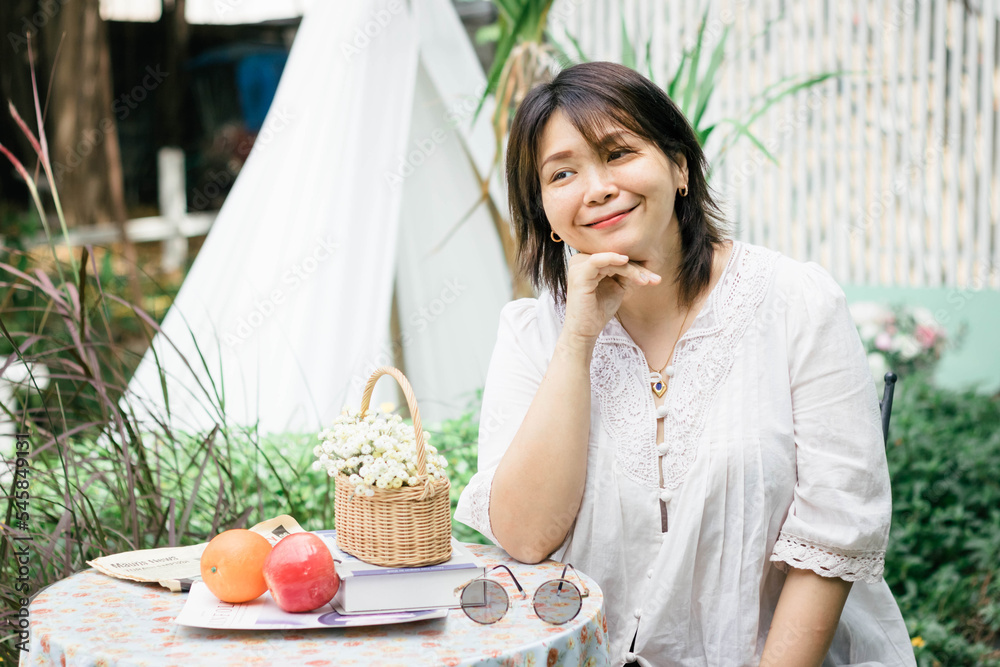 Close-up of a young pretty Asian woman sitting at a cafe, with a flower basket and decorations. Close-up of a young pretty Asian woman sitting at a cafe, with a flower basket and decorations.