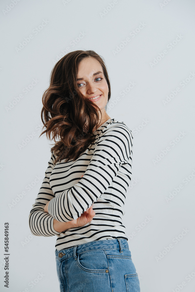 Portrait of a brunette woman with her hair on one side, body turned sideways, hands crossed. Over white wall. Portrait of a brunette woman with her hair on one side, body turned sideways, hands crossed. Over white wall.