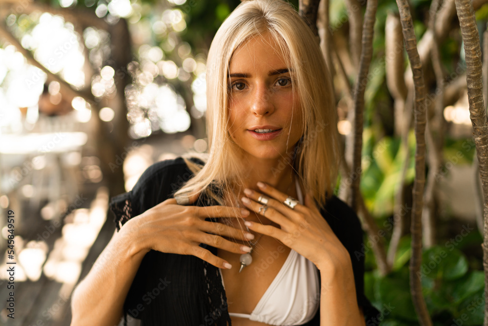 Close up portrait of pretty blond woman in boho stylish outfit posing outdoor in tropical garden. Stylish bohemian accessories. Close up portrait of pretty blond woman in boho stylish outfit posing outdoor in tropical garden. Stylish bohemian accessories.