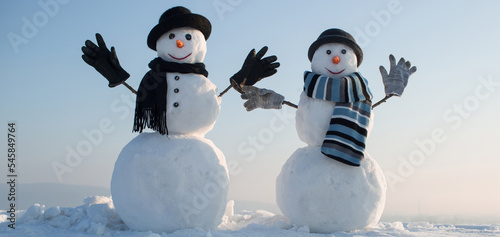 Snowmen holding hands outdoors. Winter snowman in black hat, scarf and gloves. Christmas winter banner with snowman. Winter greeting card with with snowman.