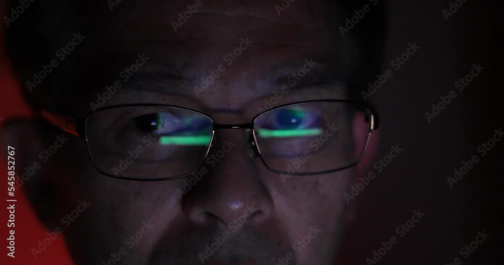 Close up view of focused middle-aged man wears computer glasses for reducing eye strain blurred vision looking at pc screen with computer reflection using internet, reading, trading. Close up view of focused middle-aged man wears computer glasses for reducing eye strain blurred vision looking at pc screen with computer reflection using internet, reading, trading.