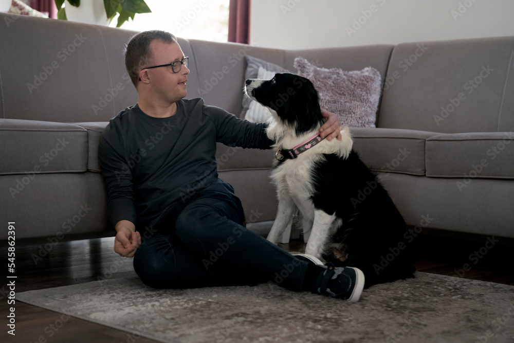 Caucasian man with down syndrome sitting on floor and playing with pet dog Caucasian man with down syndrome sitting on floor and playing with pet dog