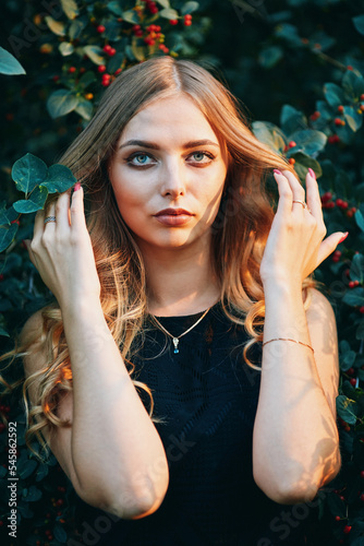Young beautiful woman in black dress looks at the camera. Outdoor portrait in the evening park