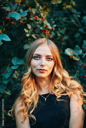 Young beautiful woman in black dress looks at the camera. Outdoor portrait in the evening park