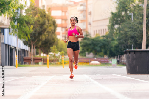 latin sportswoman running on the city's athletics track during her training, urban sport and healthy lifestyle concept, copy space for text