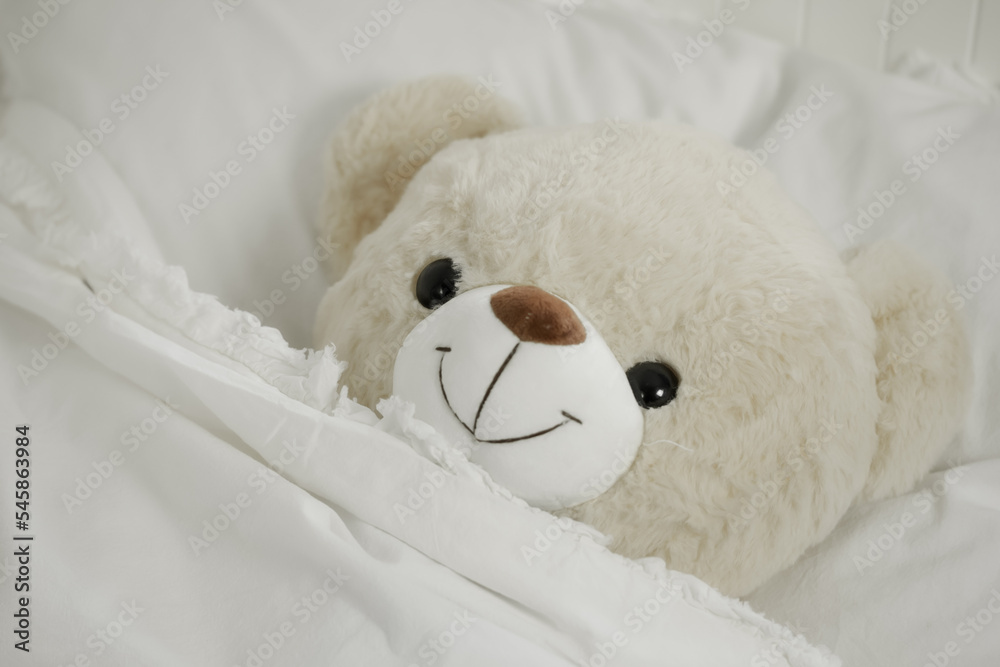 Cute teddy bear lying in the bed. A teddy bear lying on the pillow and smiling, close up