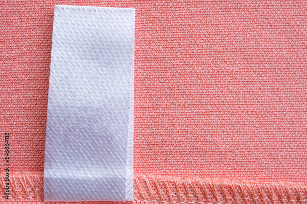 Fototapeta premium Blank white laundry care clothes label on pink fabric texture background
