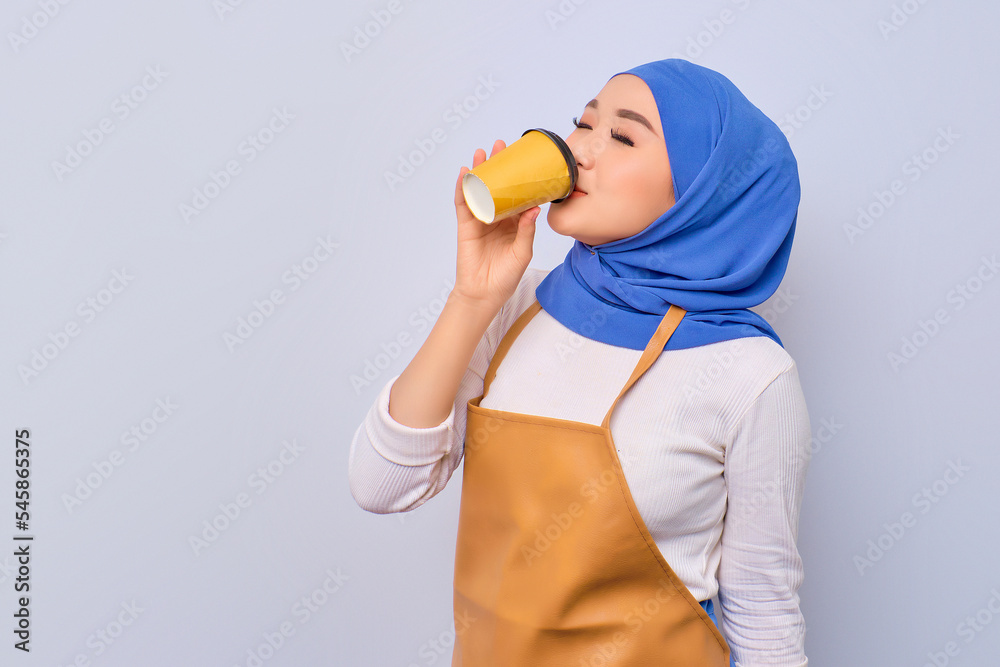 Happy pretty young barista girl in apron drinking hot coffee isolated on white background Happy pretty young barista girl in apron drinking hot coffee isolated on white background