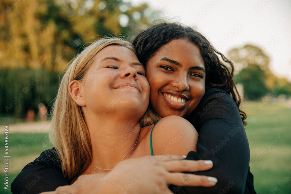 Happy teenage girl hugging female friend with eyes closed Happy teenage girl hugging female friend with eyes closed
