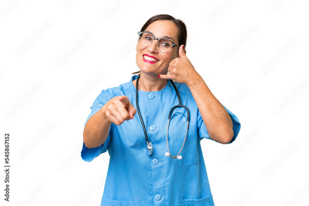 Middle-aged nurse woman over isolated background making phone gesture and pointing front Middle-aged nurse woman over isolated background making phone gesture and pointing front