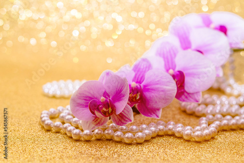 purple Orchid and pearl necklace on a shiny gold background 