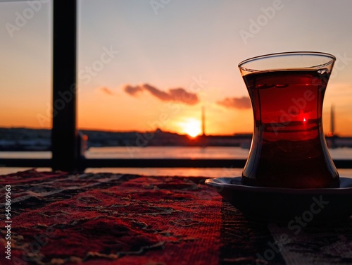 Turkish tea in Istanbul, the bridge with sunset in the background. Turkiye traditional drink in a cafe, traveling and enjoying the evening sunset in summer