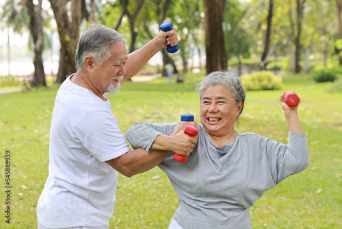 Happy and smiling asian senior couple doing arm work out and lifting dumbbell exercise with relaxation for healthy in park outdoor after retirement. Health care elderly outdoor lifestyle concept.