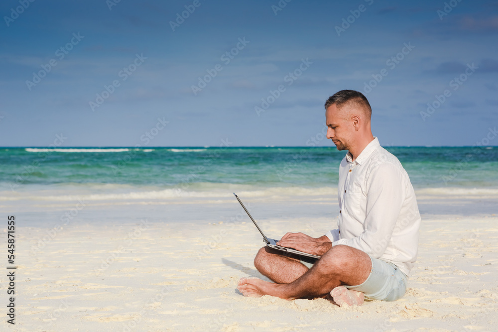 Young man using laptop computer on the beach. Relaxation Vacation Working Outdoors Beach Concept