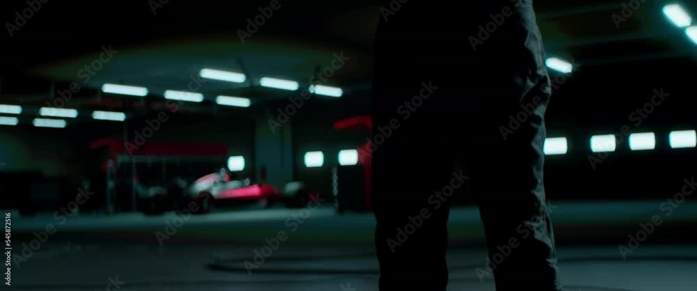 Silhouette of a racing pilot entering the pitlane garage with sports car prepared for a race