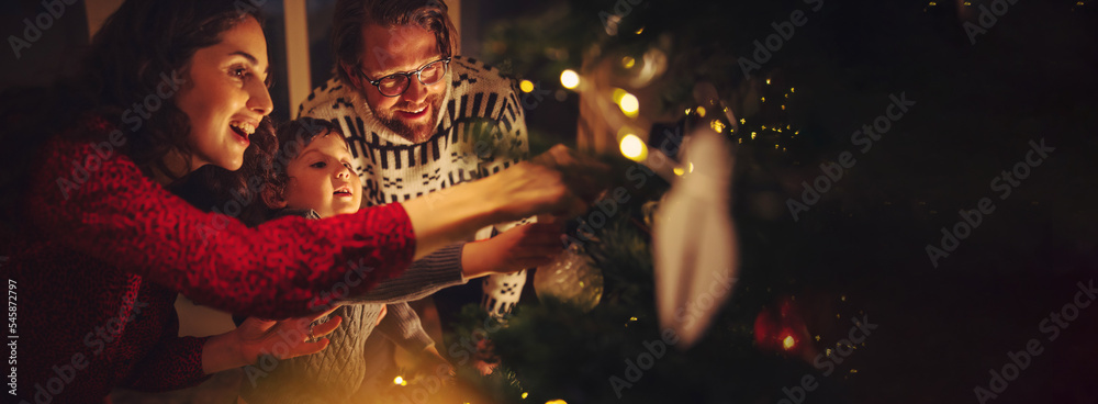 © Jacob Lund - Happy family with mother, father, and child decorate Christmas tree in a cozy warm family home during winter holidays