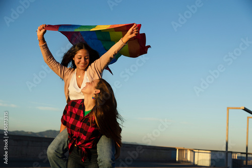 Happy lesbian young couple embraces and holds a rainbow flag. LGBT community.