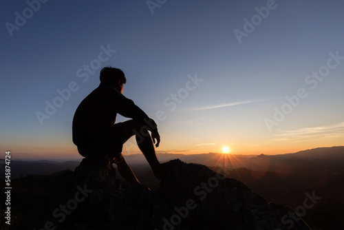 Fotografi silhouette of Sad man sitting alone on top of a mountain at sunset, Depression and loneliness