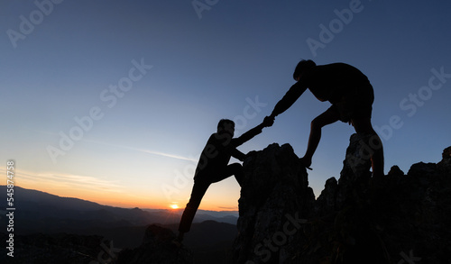 Silhouette of helping hand between two climber.  couple hiking help each other silhouette in mountains with sunlight. The men helping pull people up from high cliffs