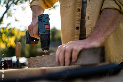 Close-up of handyman carpenter working in carpentry diy workshop outdoors with drill.