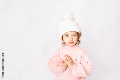 beautiful child girl on a white isolated background in a pink sweater folded cute pens as if praying, space for text