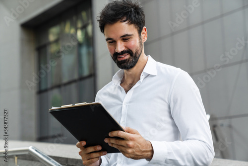 White bearded man examining papers while standing at city street