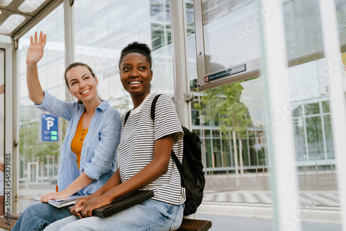 Multiracial women waving hand and smiling together while sitting at bus