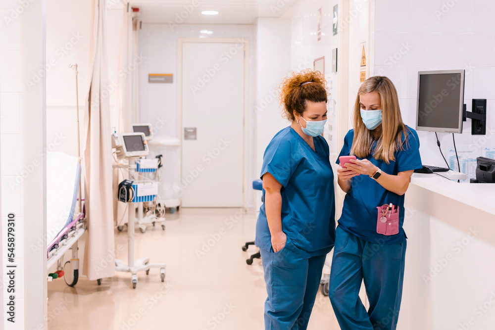 Mature nurse discussing with colleague using smart phone at medical clinic Mature nurse discussing with colleague using smart phone at medical clinic