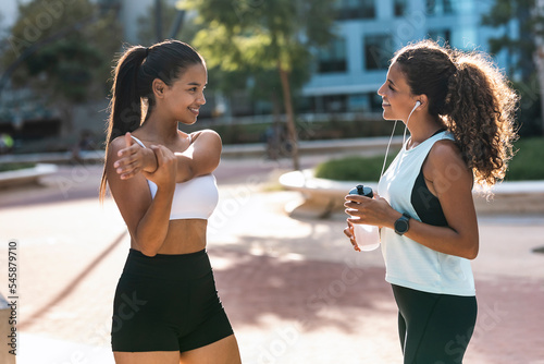 Smiling teenage girl exercising and talking to friend on sunny day