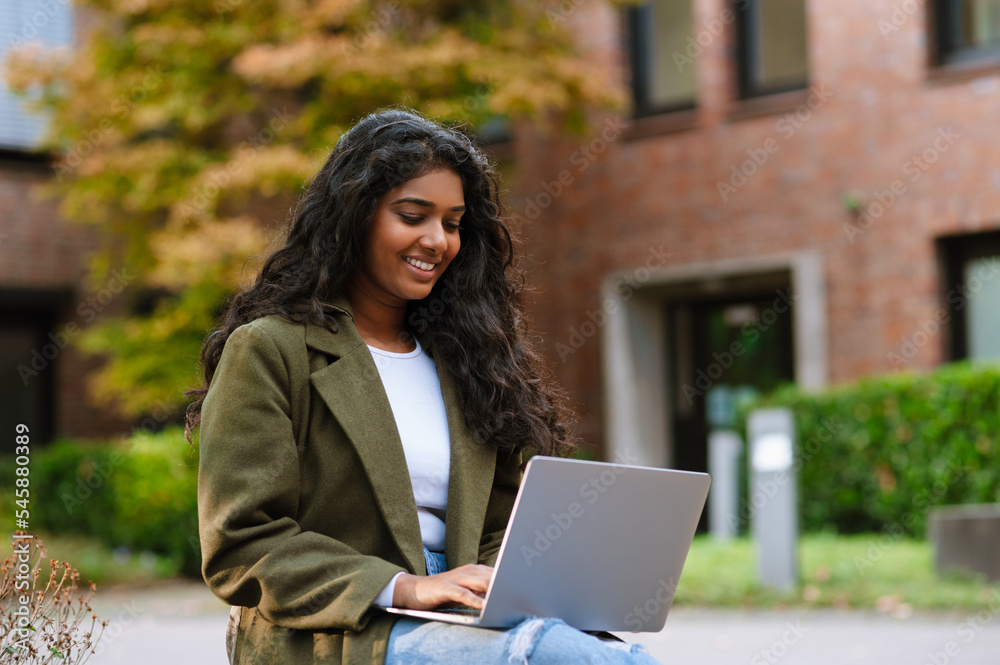 Joyful woman smiling and using laptop while sitting on city street Joyful woman smiling and using laptop while sitting on city street