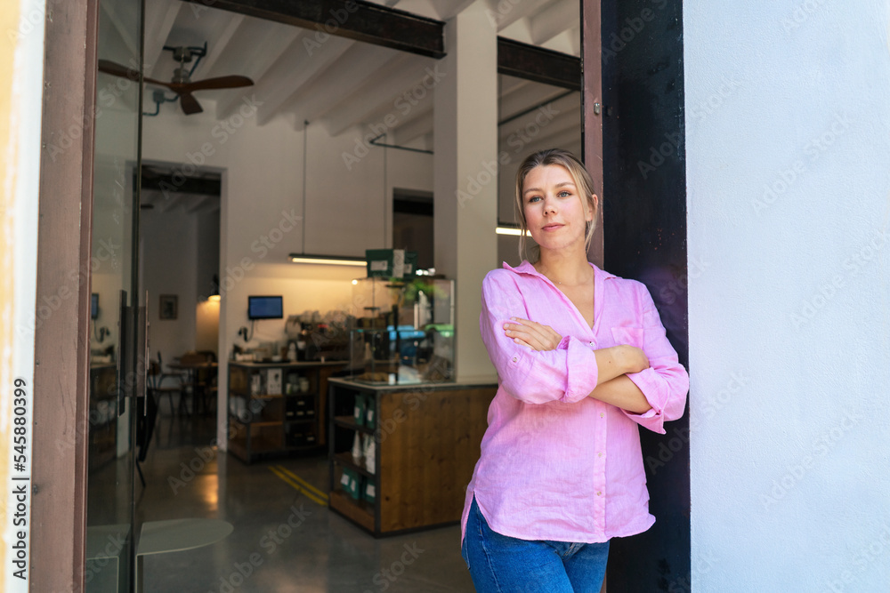 Thoughtful businesswoman with arms crossed standing in doorway at cafe Thoughtful businesswoman with arms crossed standing in doorway at cafe
