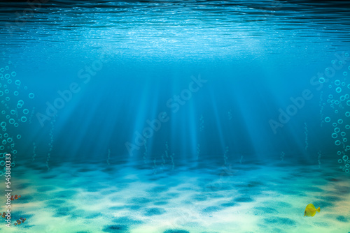 Underwater background with copy space. Blue tropical sand seabed with sunbeam and fishes.